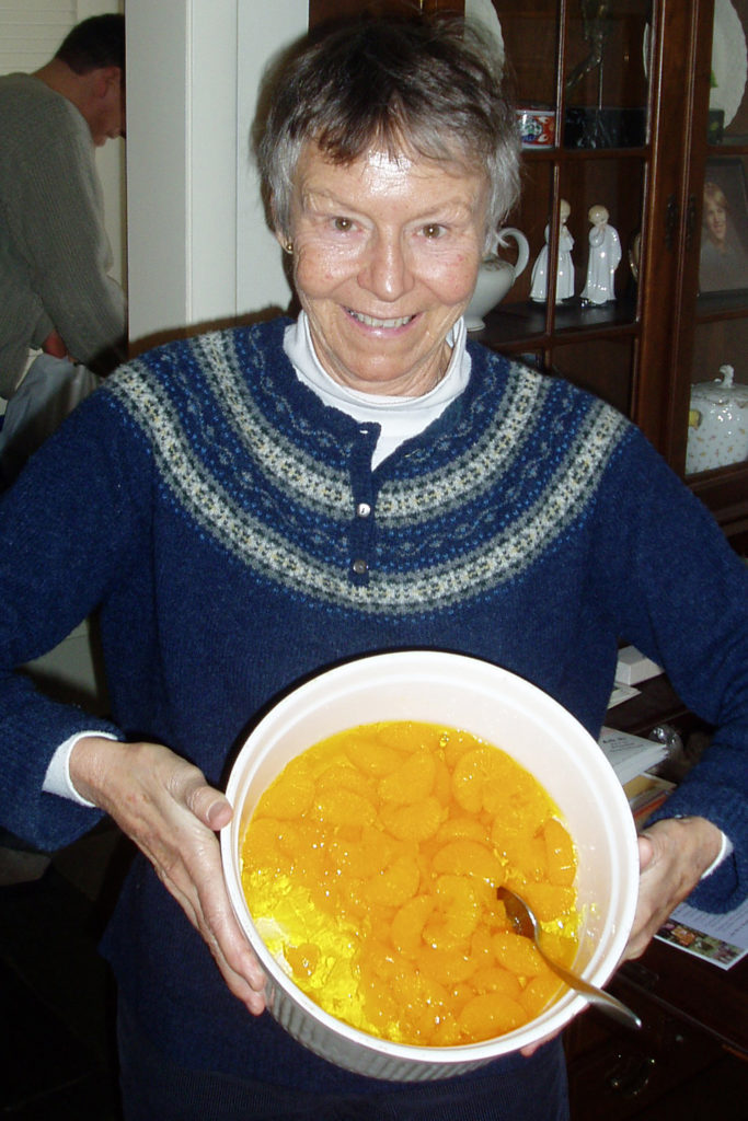 woman holding white bowl containing yellow Jell-O and probably canned mandarin orange slices