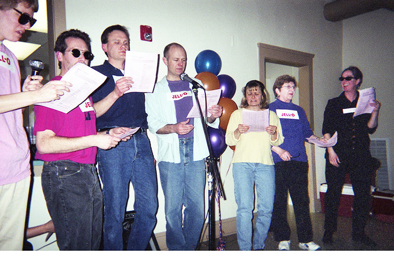 Seven people holding song sheets, singing,